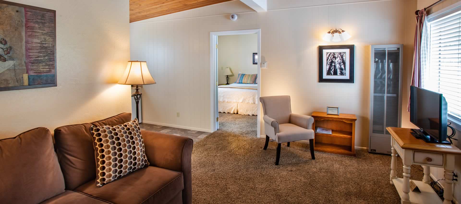 redwood-suites living room with couch, chairs, TV and doorway into bedroom